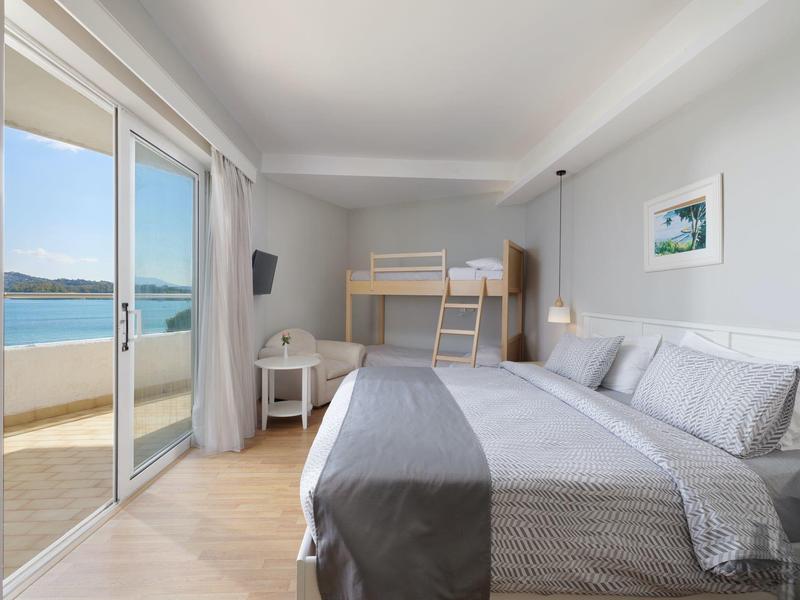 Hell eingerichtetes Schlafzimmer mit großem Bett, Etagenbett, Zugang zu Balkon und Meerblick.