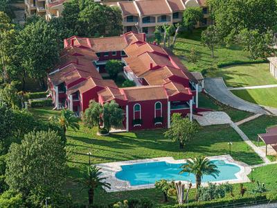 Rotes Gebäude mit Pool, umgeben von grünen Bäumen und gepflegten Wegen in Wohnanlage.