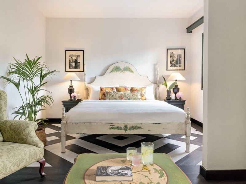 Helles Schlafzimmer mit großem Bett, grünen Pflanzen, zwei Nachttischen und schwarz-weißem Bodenmuster.