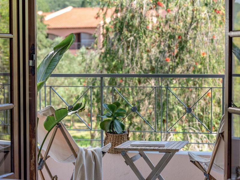 Blick auf Balkon mit zwei Holzstühlen, einer Pflanze und grüner Außenansicht mit Baum.