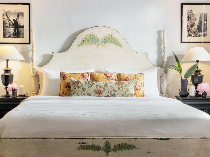 Hell eingerichtetes Schlafzimmer mit weißem Bett, dekorativen Kissen und symmetrischen Nachttischen.