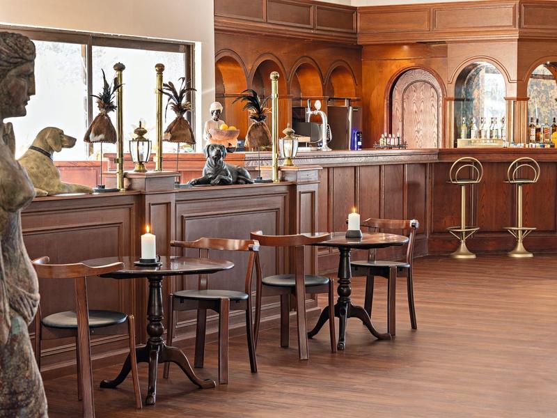 Gemütliches Café mit Holztheke, Barhockern, Tischen und Stühlen, Skulpturen und warmem Licht.