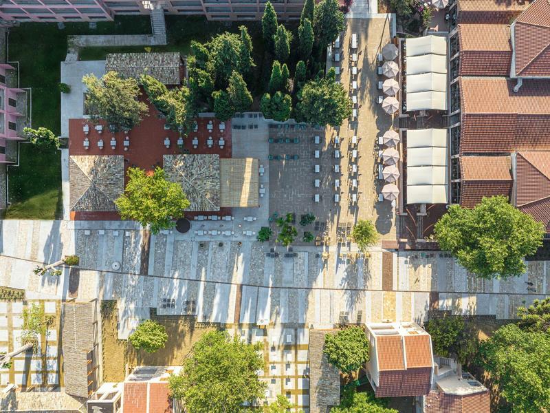 Luftaufnahme eines gepflasterten Platzes mit Sitzbereichen, Bäumen und angrenzenden Gebäuden.