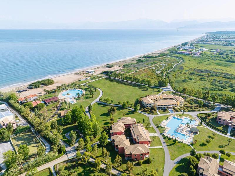 Luftaufnahme einer Küstenlandschaft mit Hotels, grünen Wiesen und mehreren blauen Schwimmbädern.