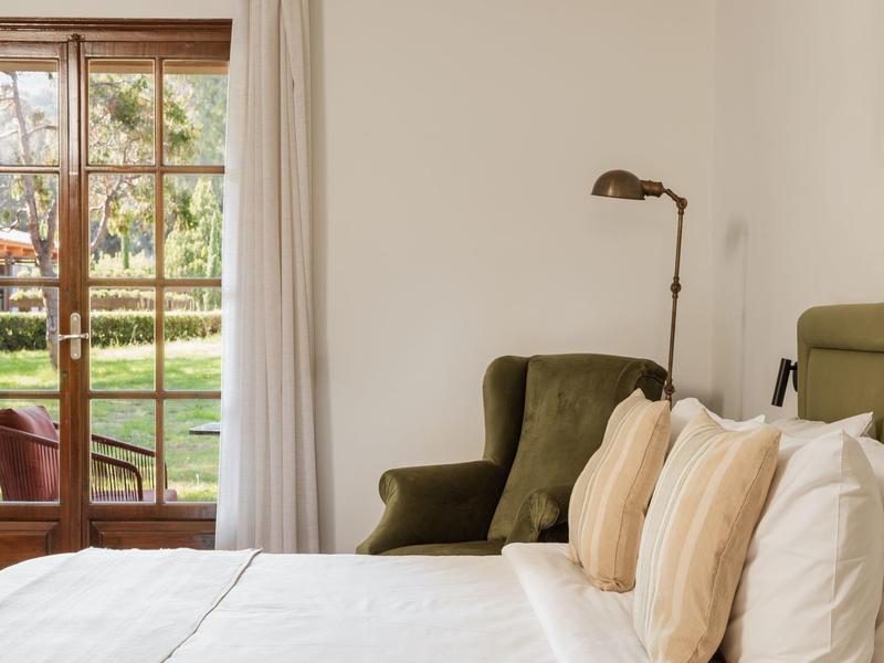 Helles Wohnzimmer mit grünem Sessel, Stehlampe, weißen und beigen Kissen und Gartentür aus Holz.