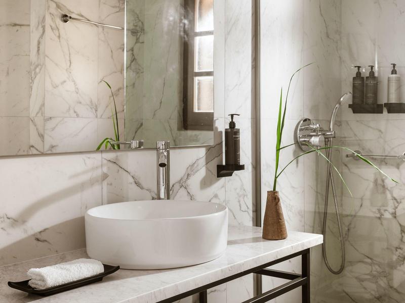 Modernes Badezimmer mit runder weißen Waschschüssel, großem Spiegel und Marmorwand.