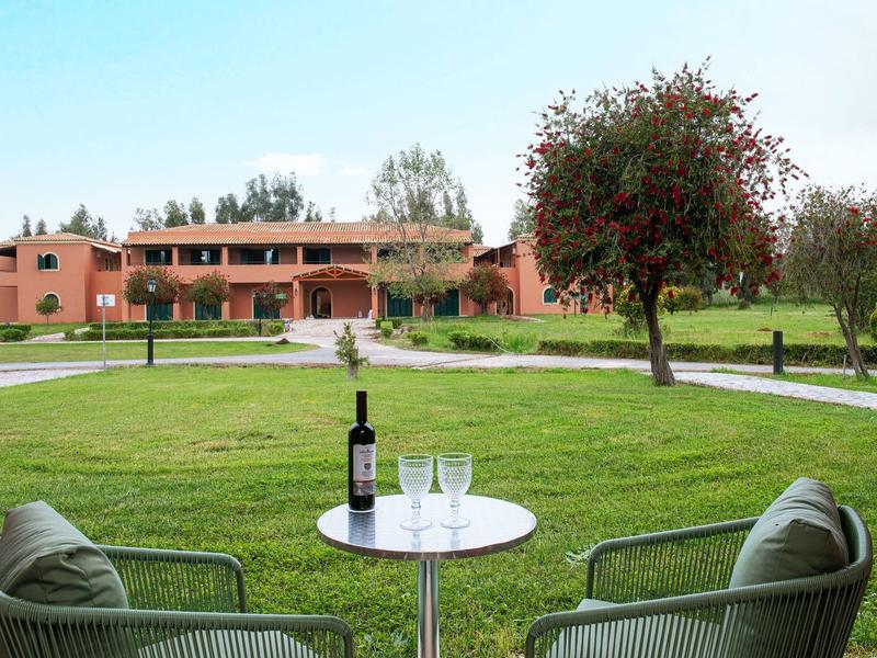 Zwei Stühle mit Kissen und ein runder Tisch mit Wein und Gläsern auf Rasen vor großem Haus.