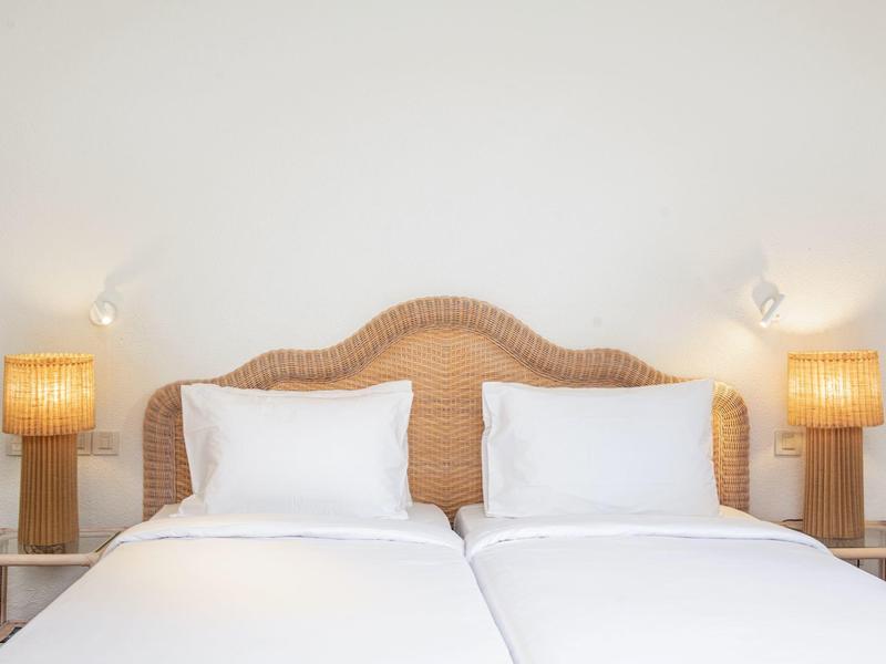 Zwei weiße Kissen und Decken auf einem Doppelbett mit geflochtenem Kopfteil und zwei Lampen.