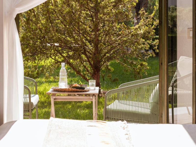 Gemütliche Terrasse mit weißem Vorhang, Tisch, Stuhl und Blick auf grünen Garten und Baum.