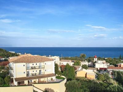 Küstenlandschaft mit Wohnhäusern, grünem Bewuchs und blauem Himmel über dem Meer.