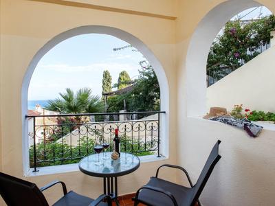 Balkon mit zwei Stühlen, rundem Glas-Tisch, Weinflasche, Meerblick und grünen Pflanzen.
