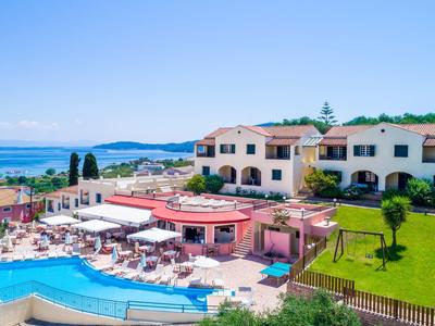 Hotelanlage mit Pool, Liegen, Sonnenschirmen, grüner Wiese und Blick auf das Meer im Hintergrund.
