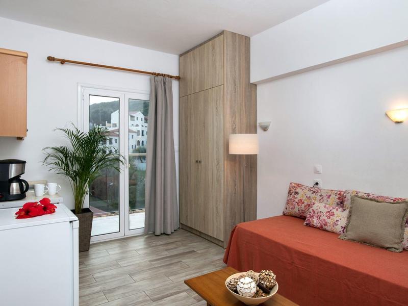 Cozy hotel room with red sofa, floral cushions, wardrobe, coffee maker, and balcony door.