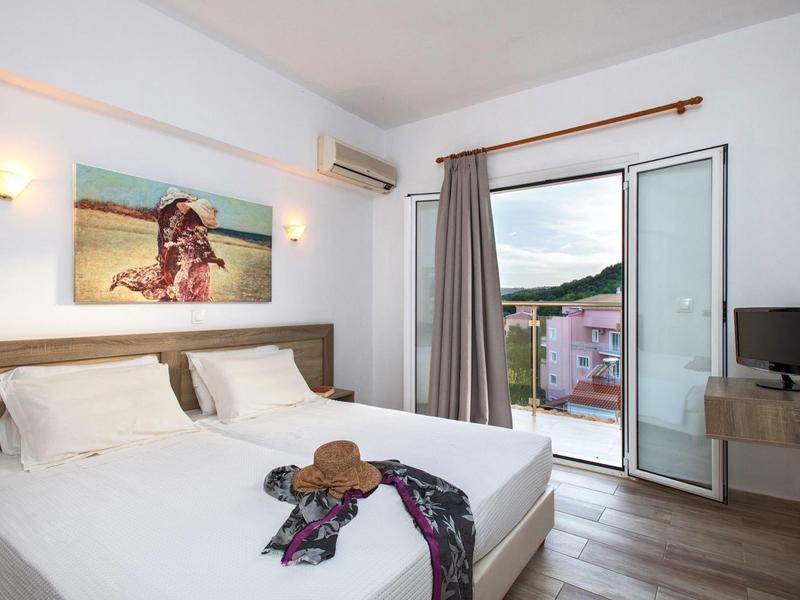 Bright hotel room with double bed, wall art, open balcony door, and bedside table with TV.