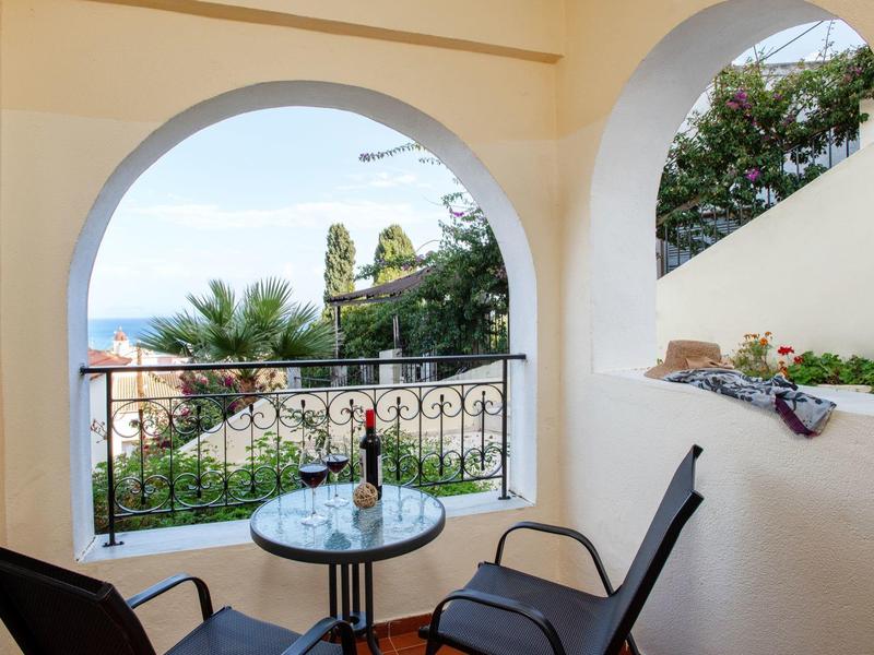 Balcony with chairs and table overlooking greenery and sea through arches.