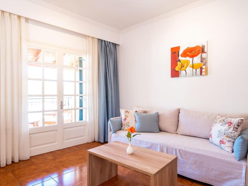Living room with light sofa, wooden table, colorful cushions, and curtained glass door.