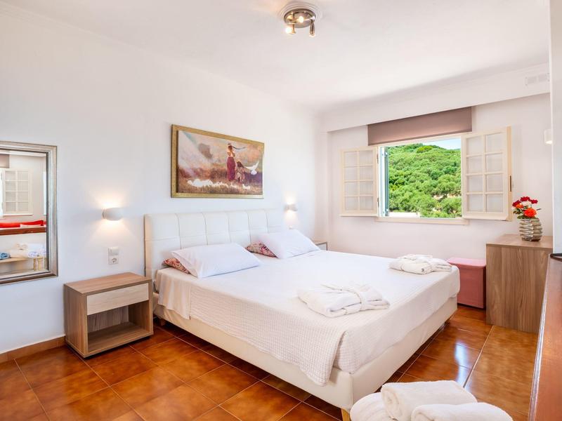 Bright hotel room with double bed, wooden furniture, and large window overlooking greenery.