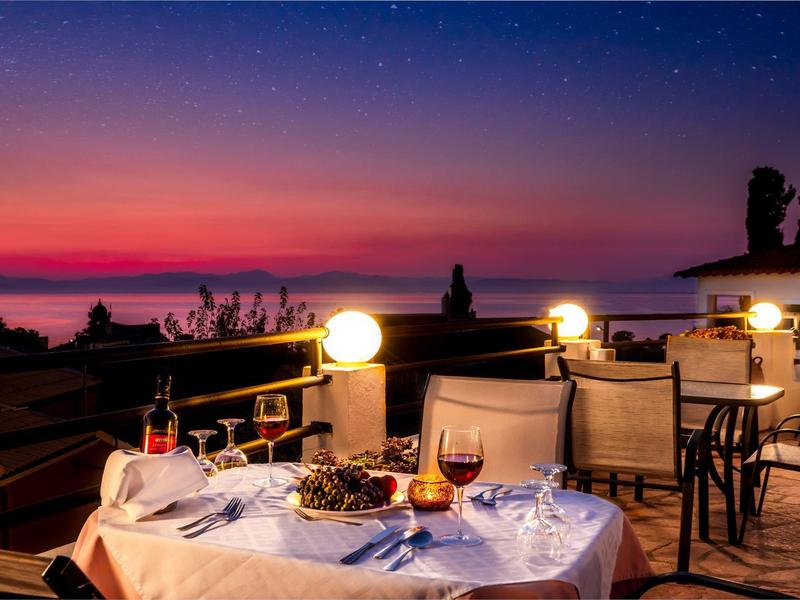 Cozy outdoor dining setup at sunset with sea view and illuminated tables.