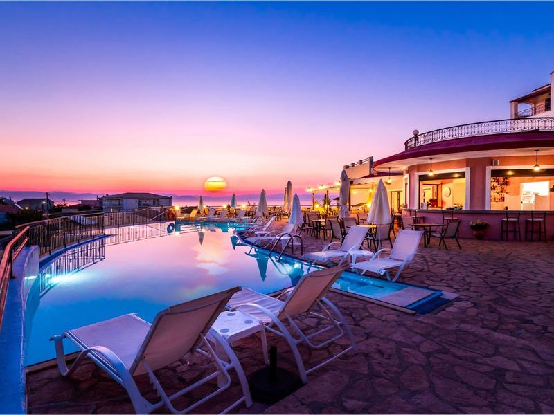 Sunset over hotel pool with lounge chairs and building illuminated in warm lights.