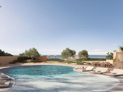 Hotelpool mit Liegestühlen, umgeben von Bäumen, mit Meerblick unter klarem Himmel.