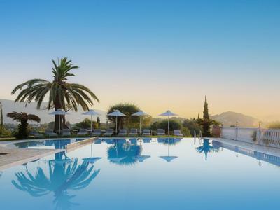 Großer Swimmingpool mit Palmen, Sonnenschirmen und klar blauem Himmel bei Sonnenuntergang.