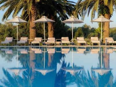 Zona tranquila de piscina con tumbonas y sombrillas frente a palmeras al atardecer.
