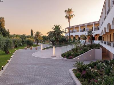 Gran edificio de hotel con arcos curvos, palmeras y un camino pavimentado al atardecer.