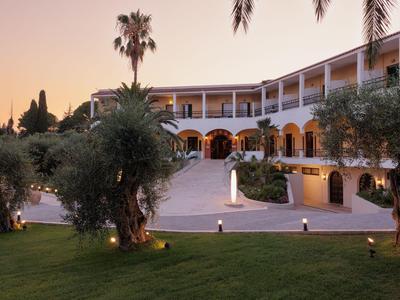 Edificio del hotel al atardecer con jardín cuidado y caminos iluminados.