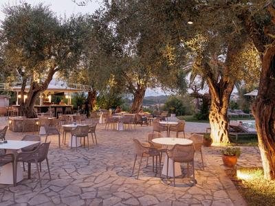 Restaurante al aire libre con mesas y sillas bajo olivos al atardecer.