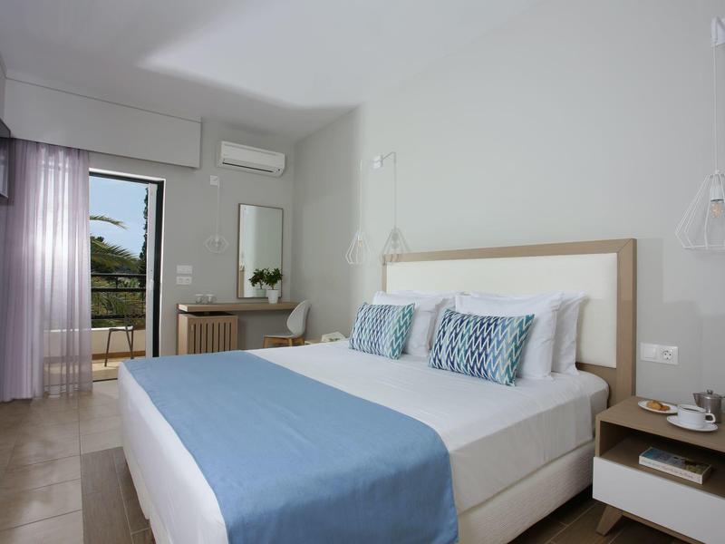 Helles Schlafzimmer mit großem Bett, blauer Decke, Nachttisch und Balkon mit Blick ins Freie.