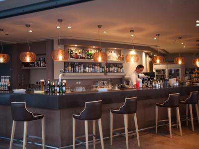 Moderner Barbereich mit Holzstühlen, beleuchteten Regalen und einem Barkeeper hinter der Theke.