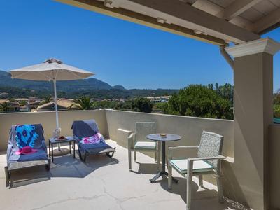 Balkon mit zwei Liegestühlen, kleinem Tisch, Sonnenschirm und Bergblick bei klarem Himmel.