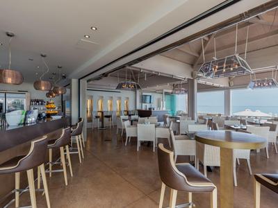 Modernes Restaurant mit braunen Stühlen, Tischen und Panorama-Meerblick bei Tageslicht.