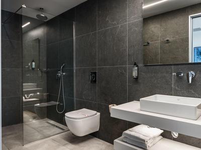 Modernes Badezimmer mit dunklen Wandfliesen, Glas-Dusche, wandhängendem WC und weißem Waschbecken.