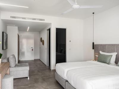 Helles Hotelzimmer mit Doppelbett, grauem Kopfteil, Schreibtisch, Sessel und minimalistischer Dekoration.
