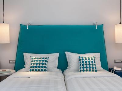 Zimmer mit zwei Einzelbetten, türkisfarbenem Kopfteil und modernen Pendelleuchten im Hotel.