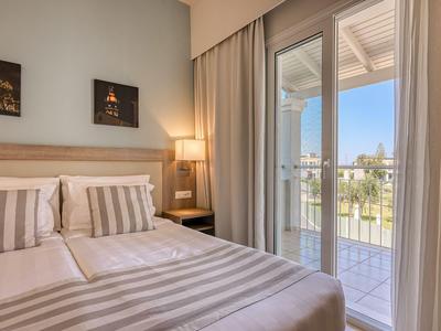Ein Hotelzimmer mit einem Doppelbett, gestreifter Bettwäsche und Balkon mit Blick auf einen Garten.