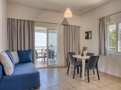 Modernes Wohnzimmer mit blauer Couch, Esstisch und Blick auf Balkon in einem Hotelzimmer.