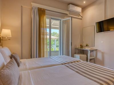 Hell eingerichtetes Hotelzimmer mit zwei Betten und Zugang zu einem Balkon mit Blick auf Grünflächen.