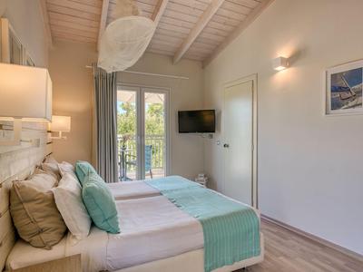 Helles Hotelzimmer mit Doppelbett, Holzdecke und Zugang zu einem Balkon mit Gartenblick.