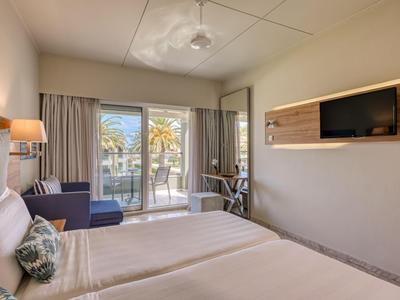 Heller Hotelzimmer mit Doppelbett, Balkon und Meerblick, moderne Einrichtung.