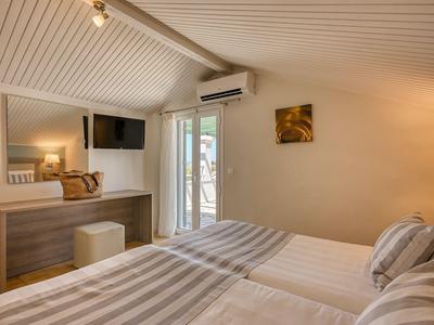 Helles Hotelzimmer mit Doppelbett, Kommode, Wandspiegel und Zugang zu Balkon oder Terrasse.