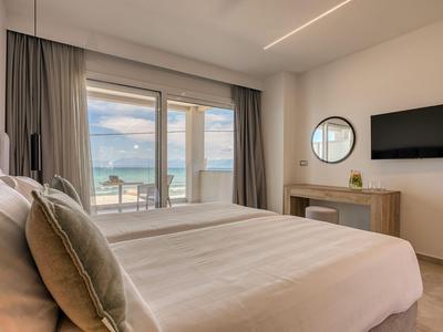 Modernes Hotelzimmer mit großem Bett, TV, Schreibtisch und Meerblick durch große Fenster.