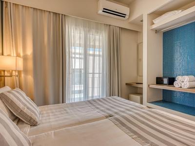 Helles Hotelzimmer mit Doppelbett, Vorhängen und Klimaanlage, moderne Einrichtung mit blauer Wand.