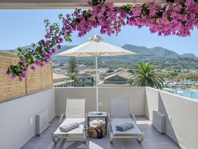 Balkon mit zwei Liegestühlen, Sonnenschirm und Blick auf Landschaft und Wasser.