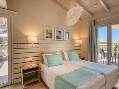 Helles Hotelzimmer mit Doppelbett, türkisfarbenen Kissen und Terrasse mit Blick.