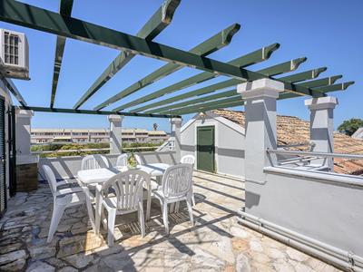 Dachterrasse mit weißem Tisch und Stühlen unter grünem Holzgitter bei klarem Himmel.