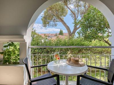 Terrasse mit rundem Tisch, zwei Stühlen und Blick auf grüne Bäume und Himmel.