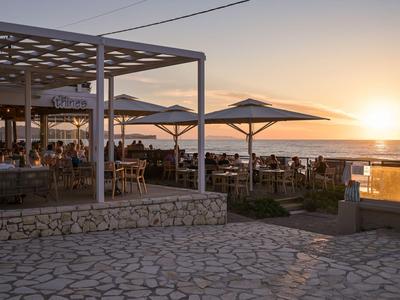 Terrasse eines Hotels mit Sitzgelegenheiten und Sonnenschirmen bei Sonnenuntergang am Meer.