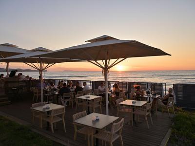 Terrasse mit Sonnenschirmen und Sitzplätzen am Meer bei Sonnenuntergang im Urlaubsort.